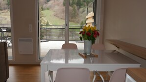 A dining area with a table, chairs, and a vase of flowers. - Apartment with large sunny terrace, close to spa and skiing (Mont-Dore)