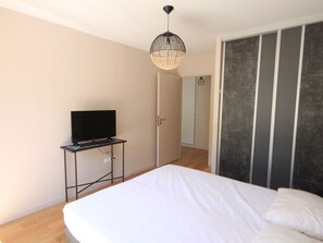 Un dormitorio con cama, televisor sobre un mueble, armario y lámpara colgante.