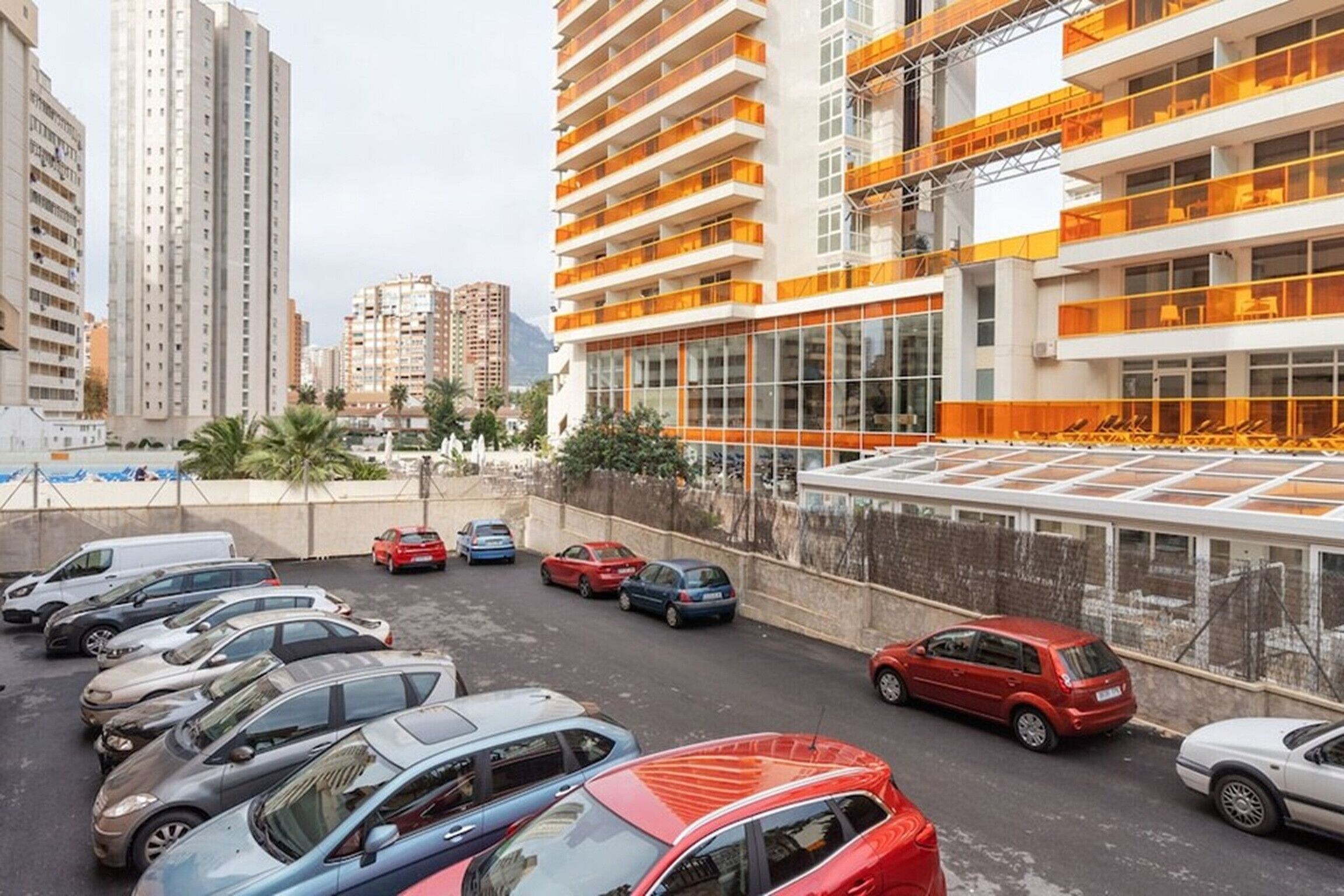 A parking lot with cars and a modern building with orange balconies.