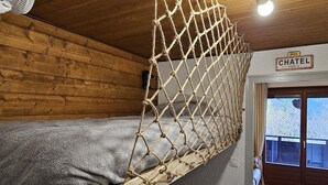 Une cabane en bois avec un lit en forme de filet de corde, une pancarte indiquant « CHÂTEL 1200 m », et une vue sur les arbres à l’extérieur.