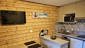 Une cuisine compacte avec un revêtement mural en bois, un téléviseur à écran plat, une machine à café et un pare-feu décoratif.