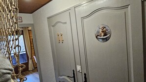 Un couloir avec une porte grise ornée d’une fenêtre circulaire représentant un petit animal, d’une poignée de porte en bois et d’un mur à texture.