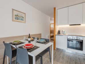 A modern kitchen with white cabinets, a built-in oven, and a dining area with a table set for two. - Central apartment with terrace, parking, 4 pers. (Chamonix-Mont-Blanc)