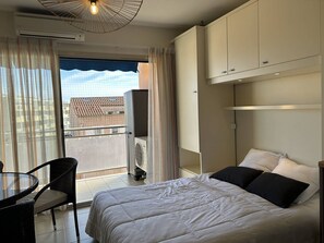 A hotel room with a bed, a chair, a table, and a view of buildings through the window. - Studio at Le Lavandou, air-conditioned, sea view terrace and Wi-Fi (Le Lavandou)