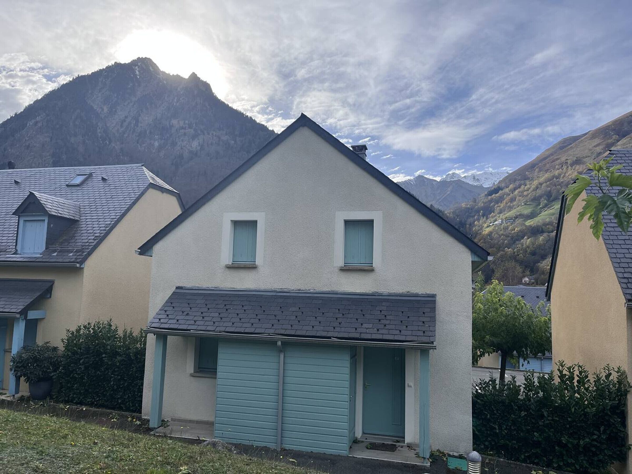 Een huis met twee verdiepingen en een garage, omringd door bergen en groen.