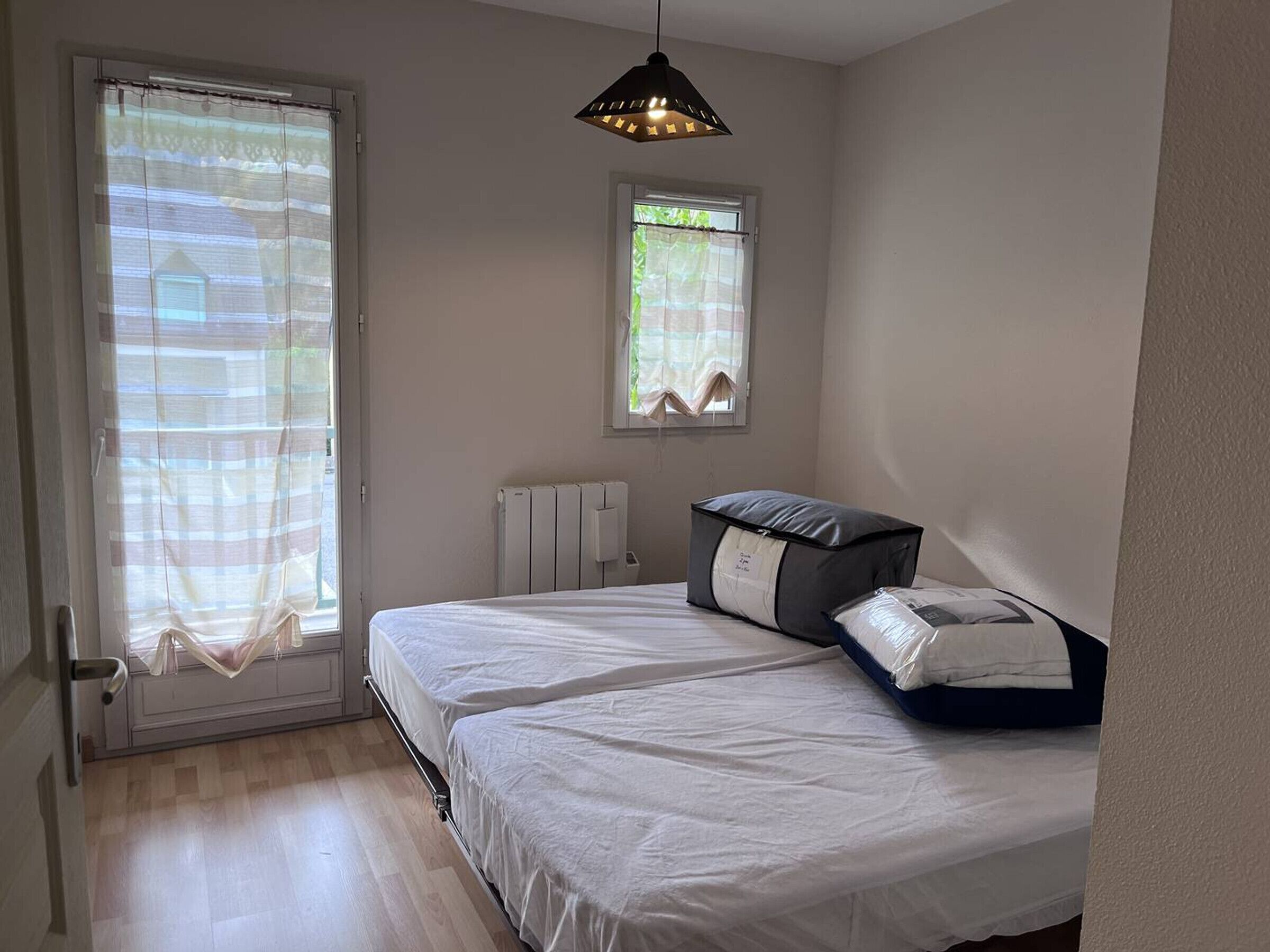 A bedroom with two beds, a radiator, a window with curtains, and a hanging light fixture.