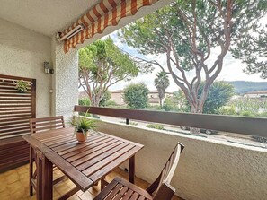 Una mesa y sillas de madera en un balcón con vistas a árboles y edificios.