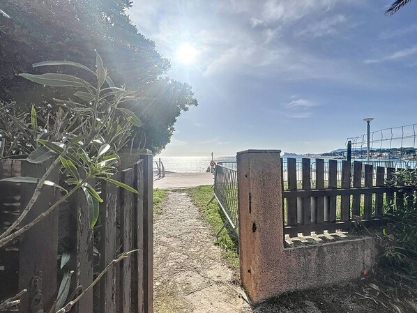 Un sentier menant à une plage, bordée d’une clôture en bois et d’une barrière en béton.
