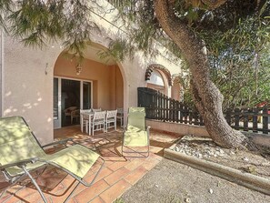 Une terrasse avec une table et des chaises, un arbre et une clôture.