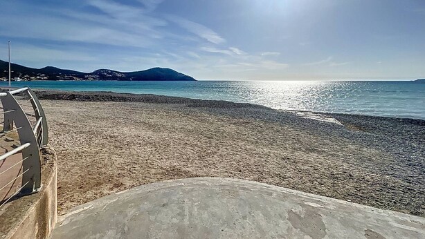 Une plage avec un ciel dégagé, une structure en béton au premier plan et une montagne lointaine.