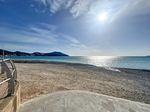 Une plage avec un ciel dégagé, une structure en béton au premier plan et une montagne lointaine.