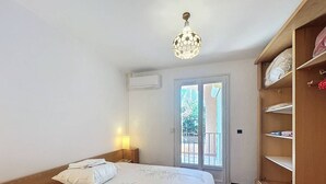 Une chambre à coucher comprenant un lit, une table de chevet, une lampe, une armoire et une porte donnant sur un espace extérieur.