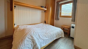 Ein Schlafzimmer mit Etagenbett, Holzwandverkleidung, einem kleinen Nachttisch und einem Fenster mit Vorhängen.