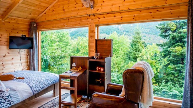 Una habitación de cabaña de madera con una cama, un escritorio, una silla y un televisor.