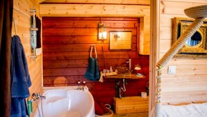 Baño de cabaña de madera con bañera, lavabo y toallero.