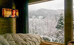 A bedroom with a bed, a television mounted on the wall, and a window offering a view of a snowy landscape. - Kedra Village Getaway - Scenic Mountain Views (Makrakomi)