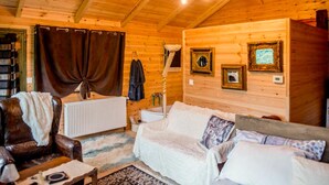 Un interior acogedor de cabaña de madera con techo de madera, un radiador blanco, un sillón de cuero, un sofá blanco y un candelabro.