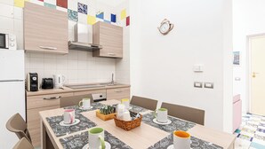 A modern kitchen with wooden cabinets, a microwave, a coffee maker, and a sink. There is a dining table with chairs and a basket of cups. - Apartment Donn'Anna Int 14 (Napoli)