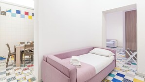 A small, neatly arranged room with a bed, a table with chairs, and a colorful tiled floor. - Apartment Donn'Anna Int 14 (Napoli)