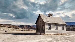 A small, single-story wooden building with a sloped roof, situated in a barren landscape with mountains in the background. - Edinbourgh 11 (Edinburgh)
