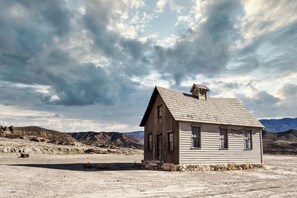 A small, single-story wooden building with a gabled roof and a chimney, situated in a barren landscape with mountains in the background. - Edinbourgh 11 (Edinburgh)