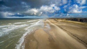 A beach with a sandy shore and a view of a distant town. - Deluxe Suite for 2 people, 80 meters, bathroom with shower and bathtub (Egmond aan Zee)