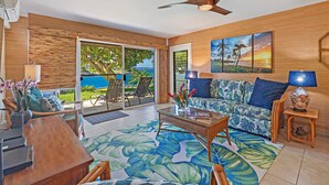 Un vaste espace de vie avec une grande fenêtre donnant sur une piscine, un canapé à motifs tropicaux et un ventilateur de plafond.