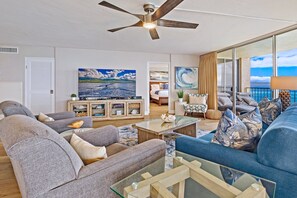 Een ruime woonkamer met een groot raam met uitzicht op zee, een plafondventilator en een gezellige zithoek met een salontafel.