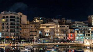 A waterfront cityscape with buildings, a dock with boats, and a pedestrian walkway. - Modern Escape Villa with Pool by ArcoCollection (St. Julian`s)