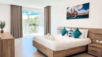 A modern hotel room with a large bed, wooden headboard, and a view of the city through large windows.