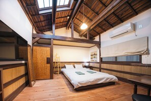 A room with a wooden ceiling, a bed with white bedding, a wooden floor, a TV on the left, and an air conditioning unit on the wall. - Shizukuan (Osaka)