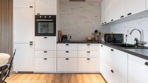 Een moderne keuken met witte kastjes, een zwarte oven, een marmeren achterwand en een zwart aanrecht.