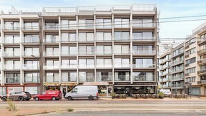 Een meerhoog gebouw met balkons, een restaurant op de begane grond en een bestelwagen ervoor geparkeerd.