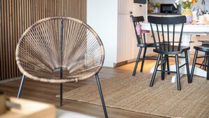 Een moderne keuken met een eethoek, met een ronde rieten stoel, zwarte stoelen en een houten vloer.