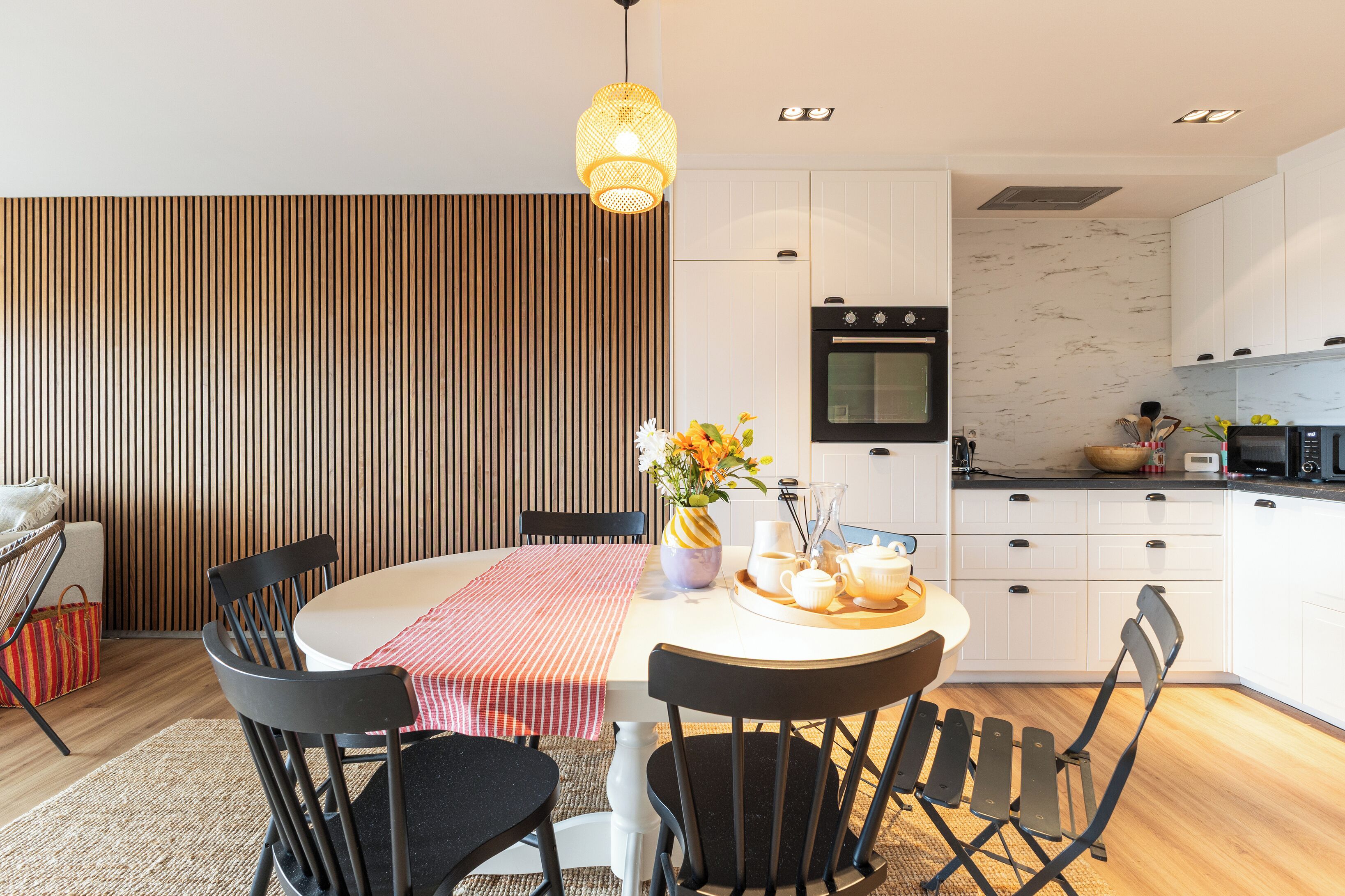 Une cuisine moderne avec des meubles blancs, un four noir et un micro-ondes. On y trouve une table à manger avec des chaises et un vase de fleurs.