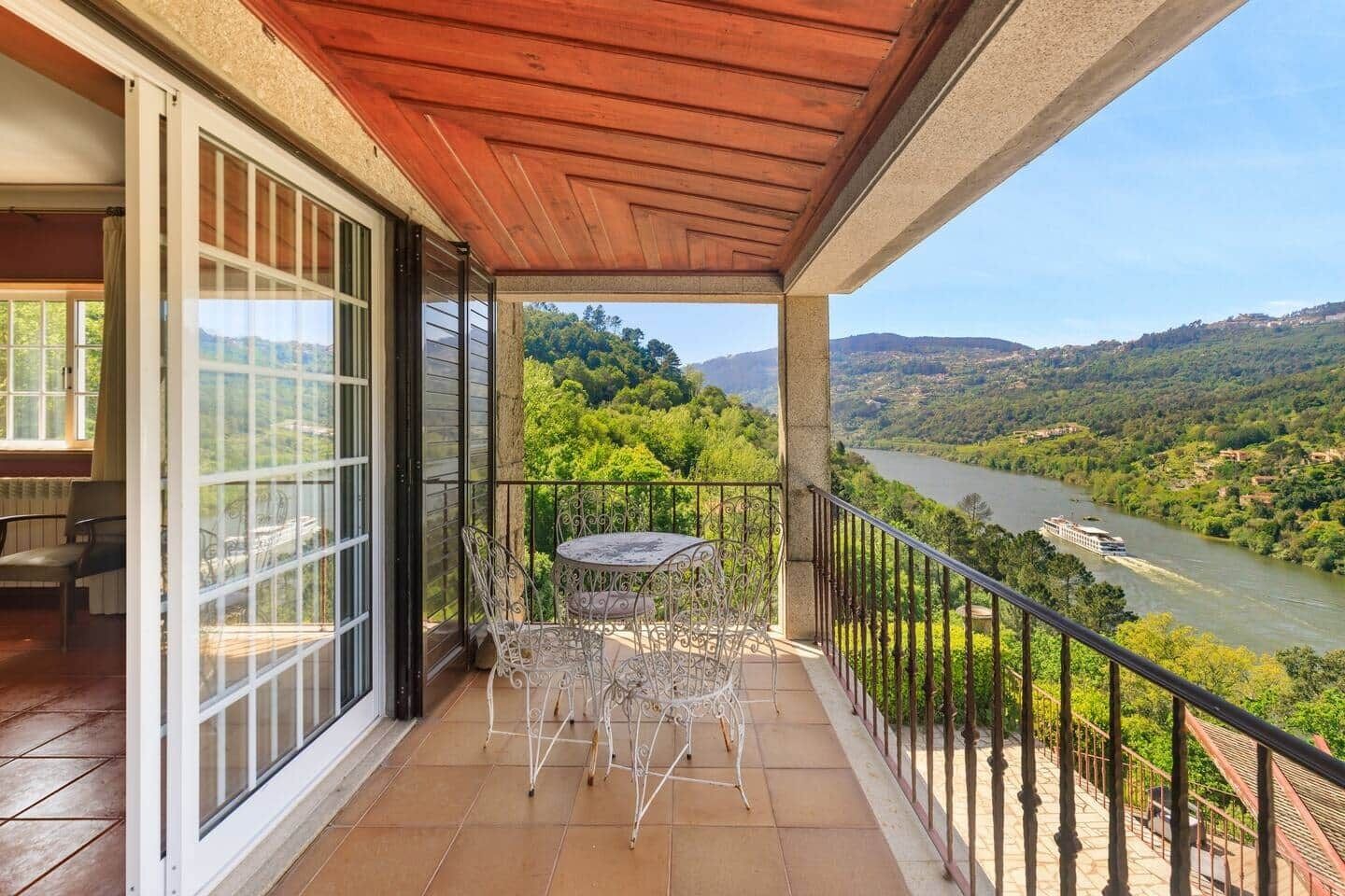 Un balcón con mesa y sillas, con vistas a un río y abundante vegetación.