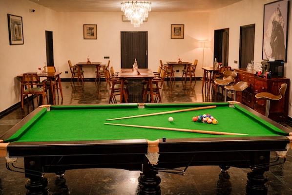 A pool table with balls, a chandelier, and a dining area with chairs and tables.