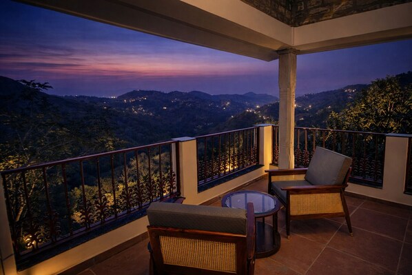 Ein Balkon mit zwei Korbstühlen und einem kleinen Tisch mit Blick auf eine gebirgige Landschaft im Abendlicht.