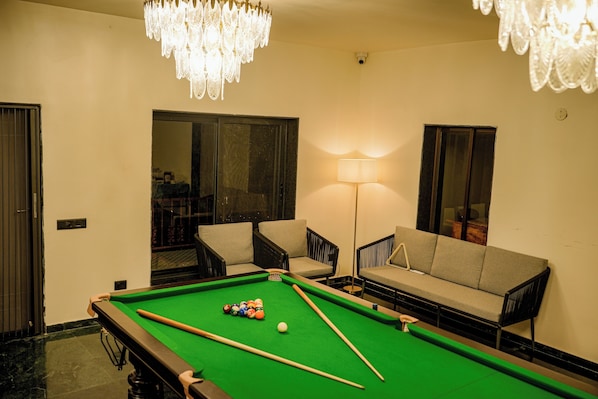 Una mesa de billar con bolas, un sofá y dos sillones en una habitación con una araña.