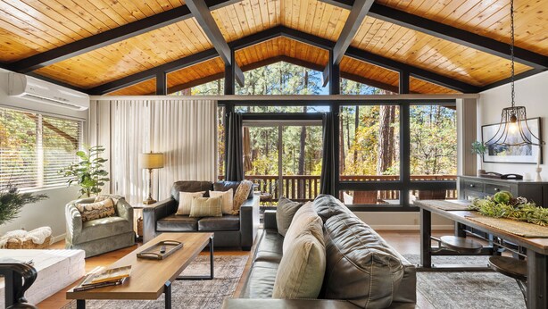 A spacious living area with a high ceiling, large windows, and a view of trees.