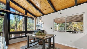 A modern interior with a wooden ceiling, large windows, a dining table with a plant, and a gray rug.