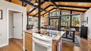 A spacious kitchen with a large island, wooden beams on the ceiling, and a view of the outdoors through large windows.