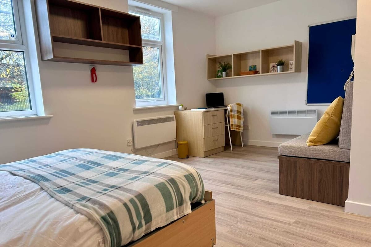 A bedroom with a bed, a desk, a chair, and a sofa.