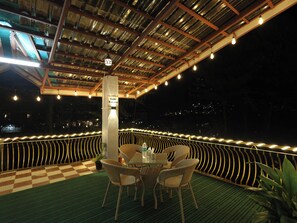 An outdoor seating area with wicker chairs and a table, a checkered floor, and string lights. - Elysian heights (Manali)