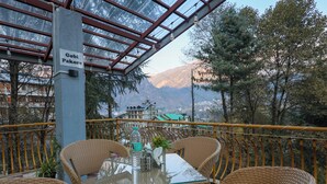 A terrace with wicker furniture, a glass table, and a view of mountains. - Elysian heights (Manali)