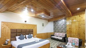 A wooden-paneled bedroom with a large bed, a sofa, and a small table with a glass top. - Elysian heights (Manali)