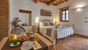Quarto aconchegante com cama, mesa de cabeceira e um espaço para café da manhã, com mesa, cadeiras e uma vela.