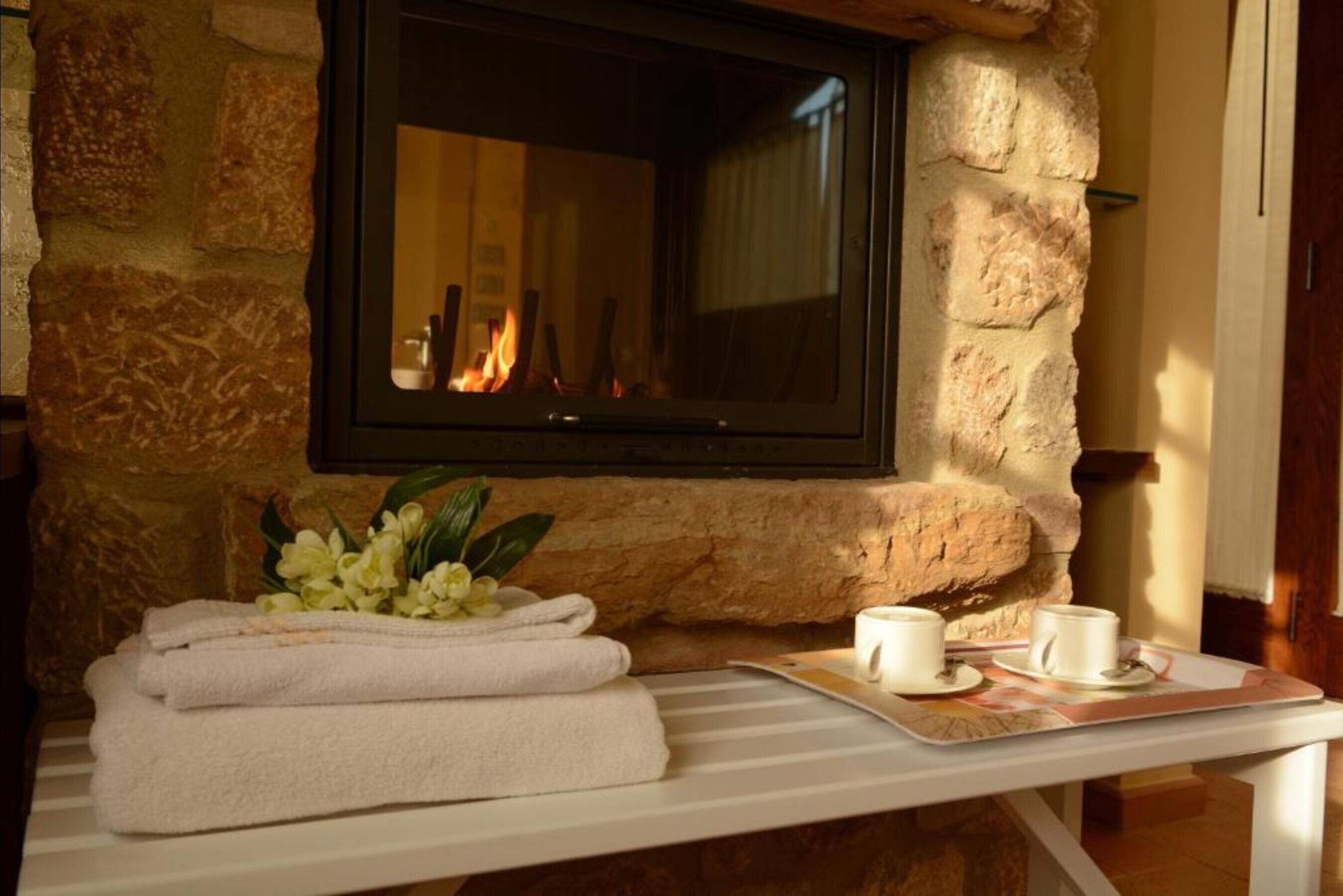 A stone wall with a fireplace, towels, and cups on a tray.