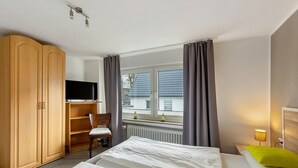 Ett hotellrum med en säng, en tv, en garderob, en stol och ett fönster med gardiner.
