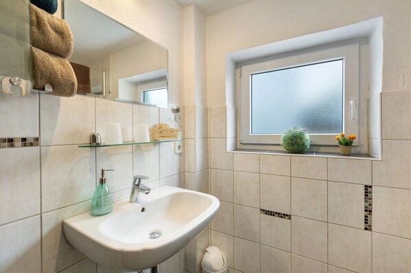 Une salle de bain équipée d’un lavabo, d’un miroir, d’un porte-serviettes, d’une fenêtre et d’une petite plante en pot.